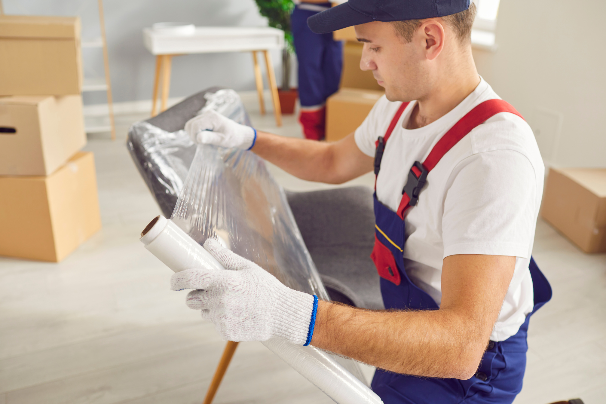 Portrait of young male mover packing furniture with plastic wrap in the living room